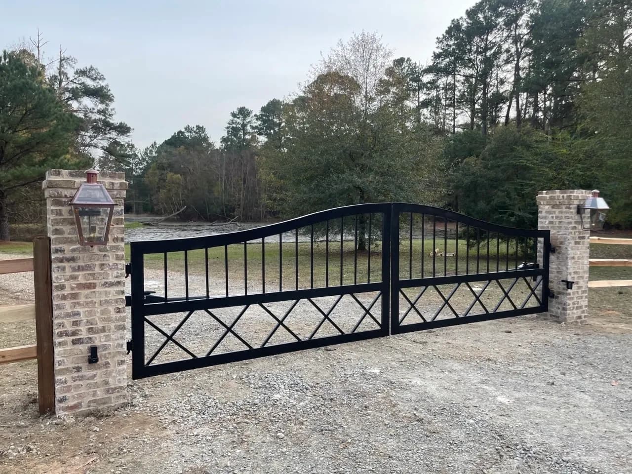 Black iron double driveway gate between brick pillars with copper lanterns