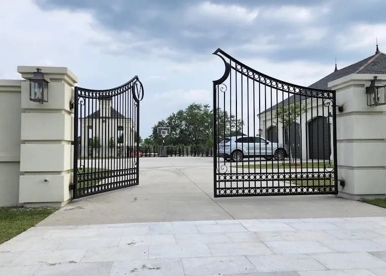 Open scrollwork iron entrance gates between stucco pillars with lanterns
