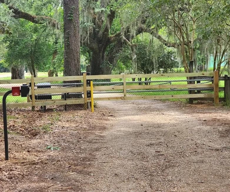 Wood ranch style gate across a gravel drive with a keypad access post